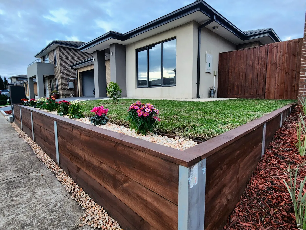 Finished raised garden showing the stained sleeper wall, pebble strip and new lawn